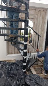 Supar Steel technicians installing a black steel spiral staircase on-site, balustrade panels being fitted